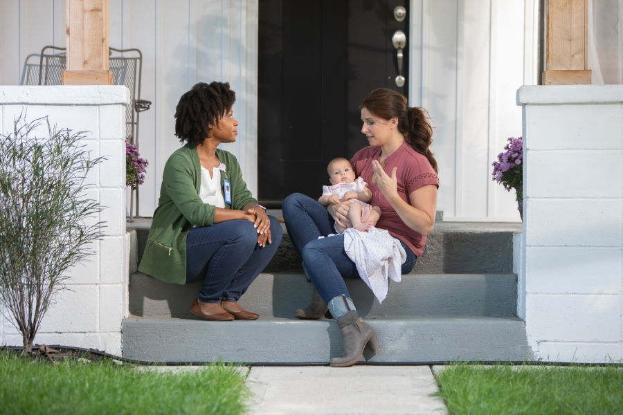 Mother with baby on porch steps talking with a family support provider